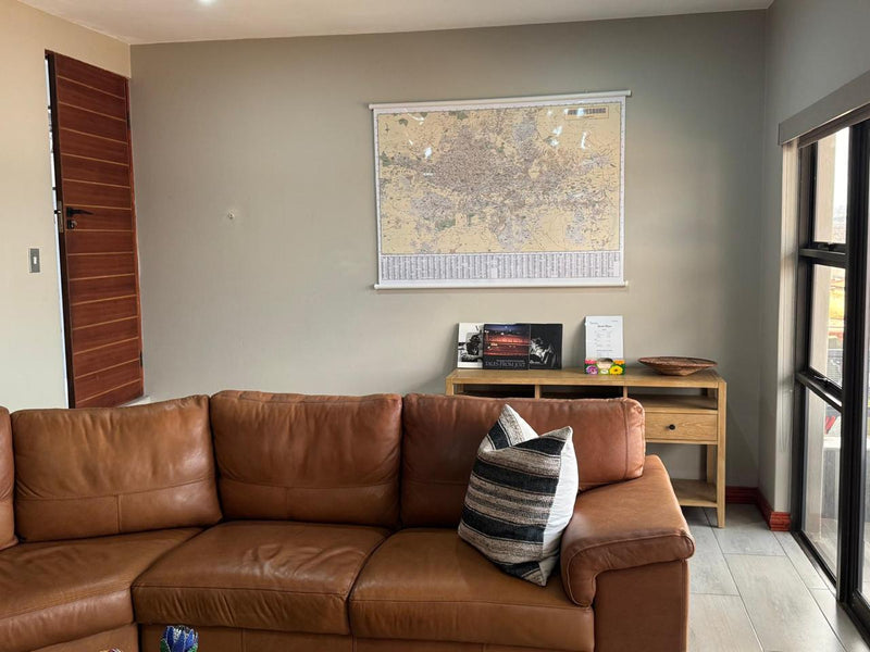 Brown leather sectional sofa in a living room with a map of Johannesburg on the wall.